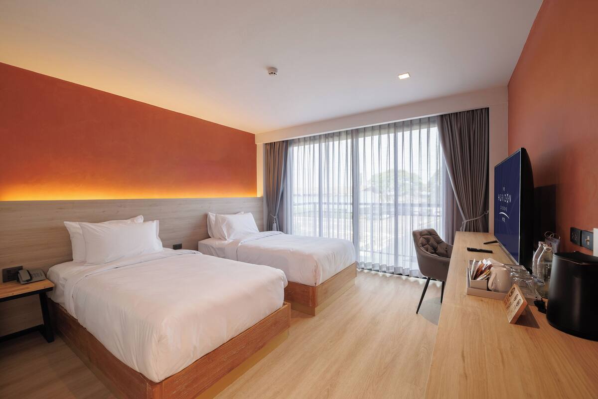 Een hotelkamer met twee bedden, een bureau, een televisie en een groot raam met gordijnen.