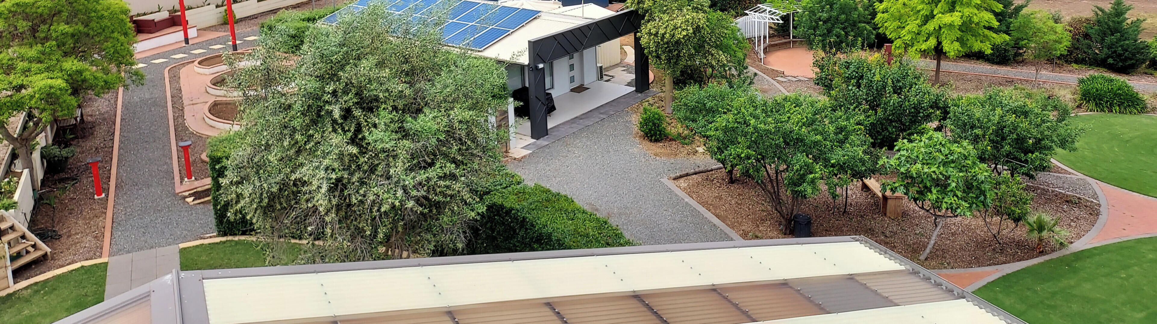A modern building with a solar panel roof, surrounded by well-maintained greenery and a paved pathway.
