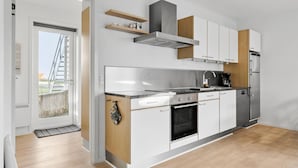 A modern kitchen with white cabinets, a stainless steel range hood, and a built-in oven. - Gudhjem Søpark Lejl. 29 (Gudhjem)