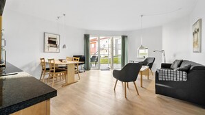 A modern living room with a dark sofa, a dining area with wooden chairs, and a kitchen with a granite countertop. - Gudhjem Søpark Lejl. 29 (Gudhjem)