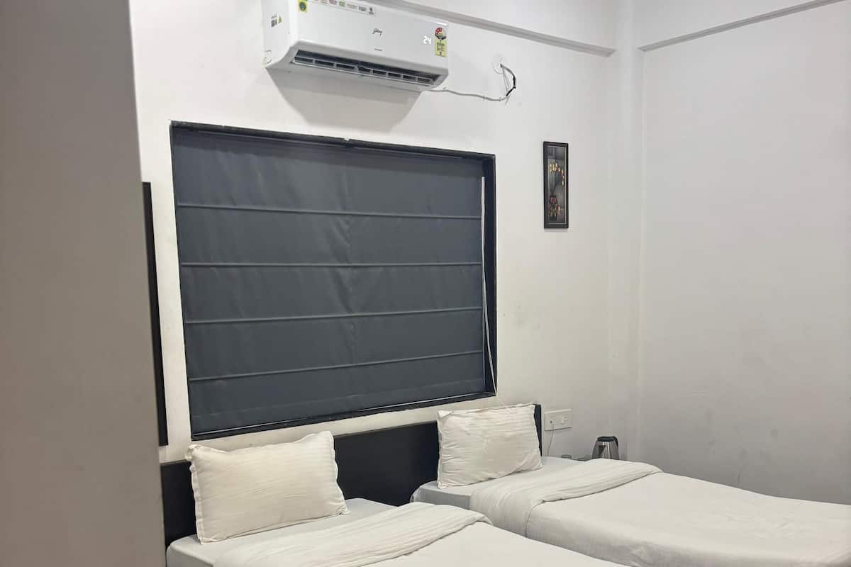 A hotel room with two single beds, a ceiling fan, an air conditioning unit, and a wooden floor.