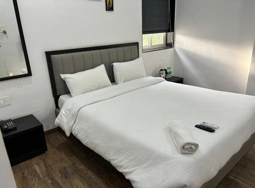 Een net opgemaakt bed met witte lakens, een grijs hoofdbord en een afstandsbediening op het bed.