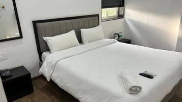 Een net opgemaakt bed met witte lakens, een grijs hoofdbord en een afstandsbediening op het bed.