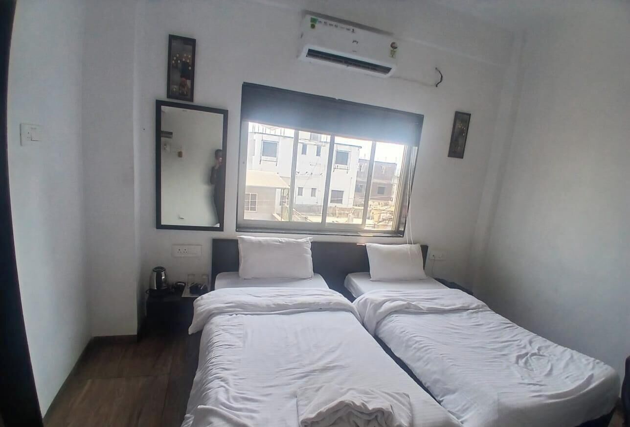 A hotel room with two beds, a large window, a mirror, and an air conditioning unit.