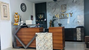A reception area with a marble wall, a clock, and a ceiling fan. - Sunny Executive Satara (Satara)