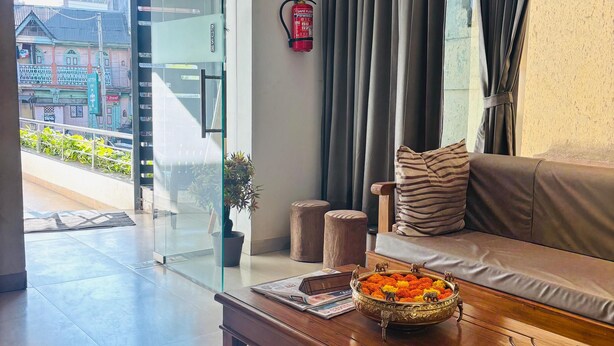 A modern living room with a sofa, a coffee table with a decorative bowl, a fire extinguisher, and a view of the street outside. - Sunny Executive Satara (Satara)