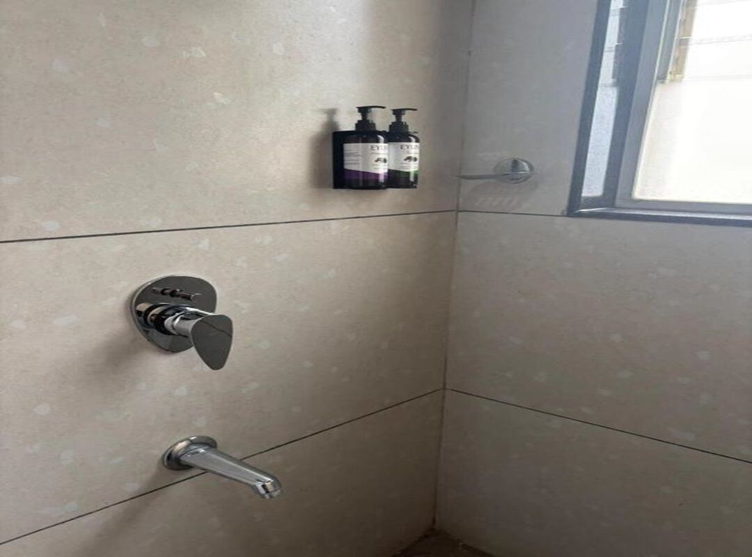 Canto de um banheiro com porta do chuveiro, porta-toalhas com frascos e uma janela.