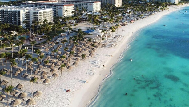 A beach resort with multiple buildings, palm trees, and a sandy shoreline.