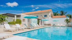 A swimming pool with lounge chairs and umbrellas, surrounded by a building with a tiled roof.
