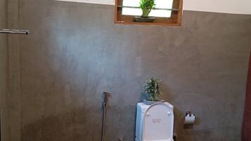 Un baño con inodoro, ducha y una ventana pequeña con una planta.