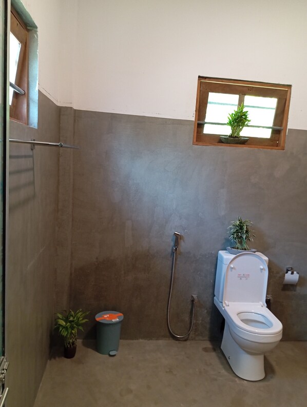 A bathroom with a shower, toilet, and a small window with a plant.