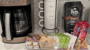 Une cuisine équipée d’une machine à café, d’une cafetière et de différents types de dosettes et de sachets de café, le tout disposé sur le comptoir.