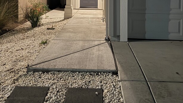 Une maison d’habitation avec une allée menant à la porte d’entrée, un garage et un petit jardin agrémenté de gravier et de plantes.