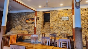 A restaurant with stone walls, wooden furniture, and a ceiling fan. - Ceylon Adventure Sport (Kitulgala)