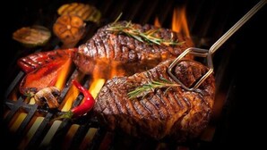 A steak being grilled with a tongs, surrounded by vegetables and a fire. - Ceylon Adventure Sport (Kitulgala)