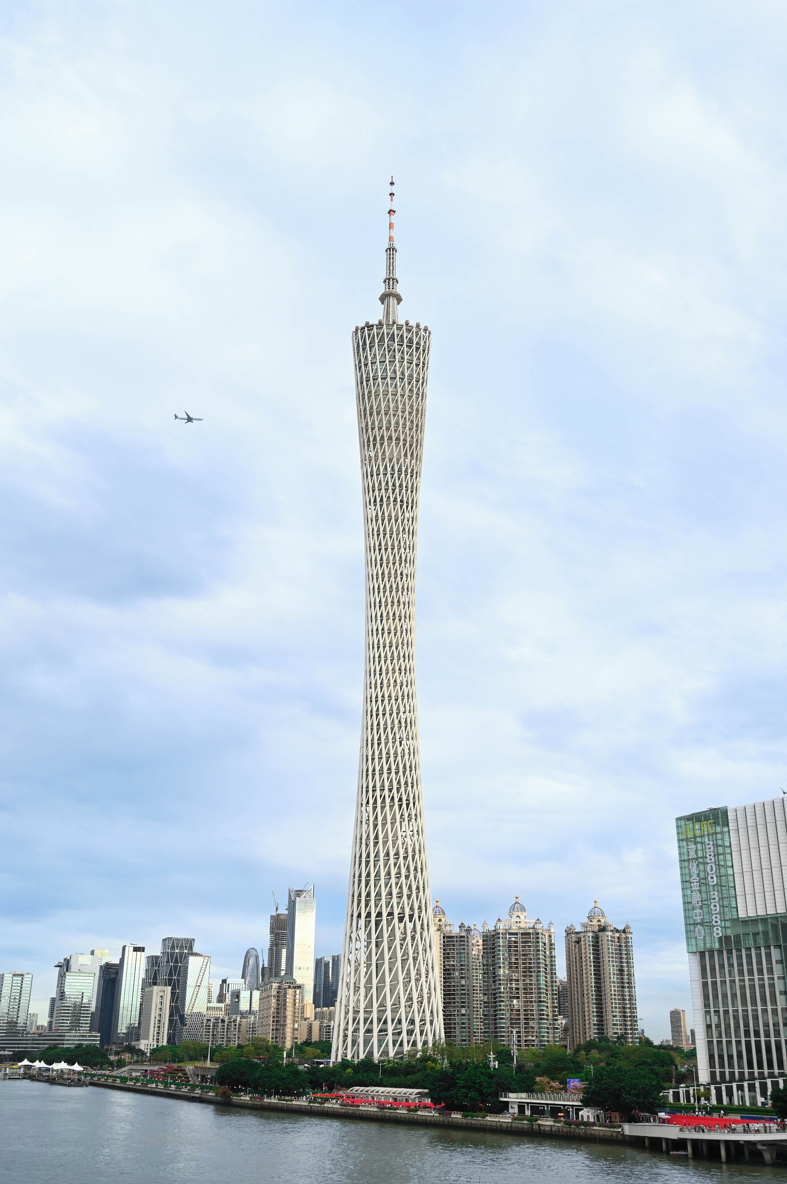 A tall, modern tower with a unique lattice structure, surrounded by a city skyline and a body of water.