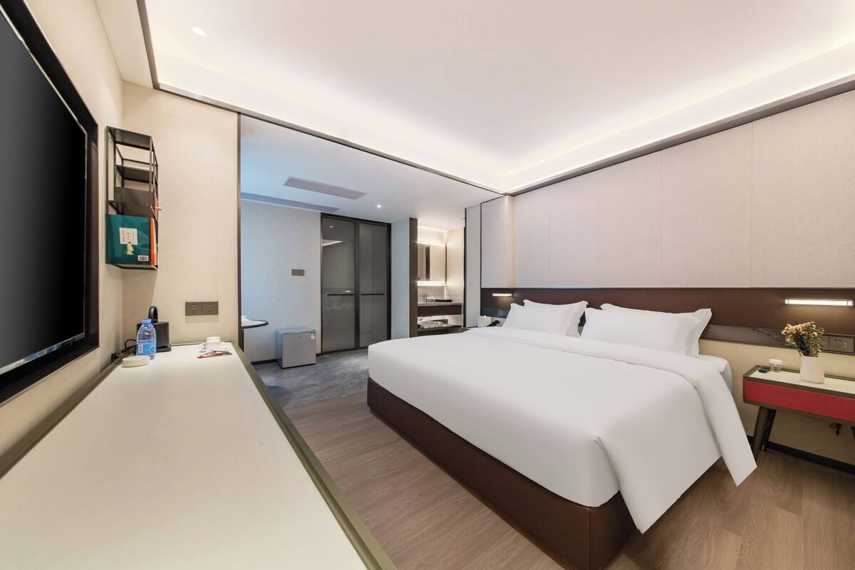 A modern hotel room with a large bed, bedside table, and a TV on the left.