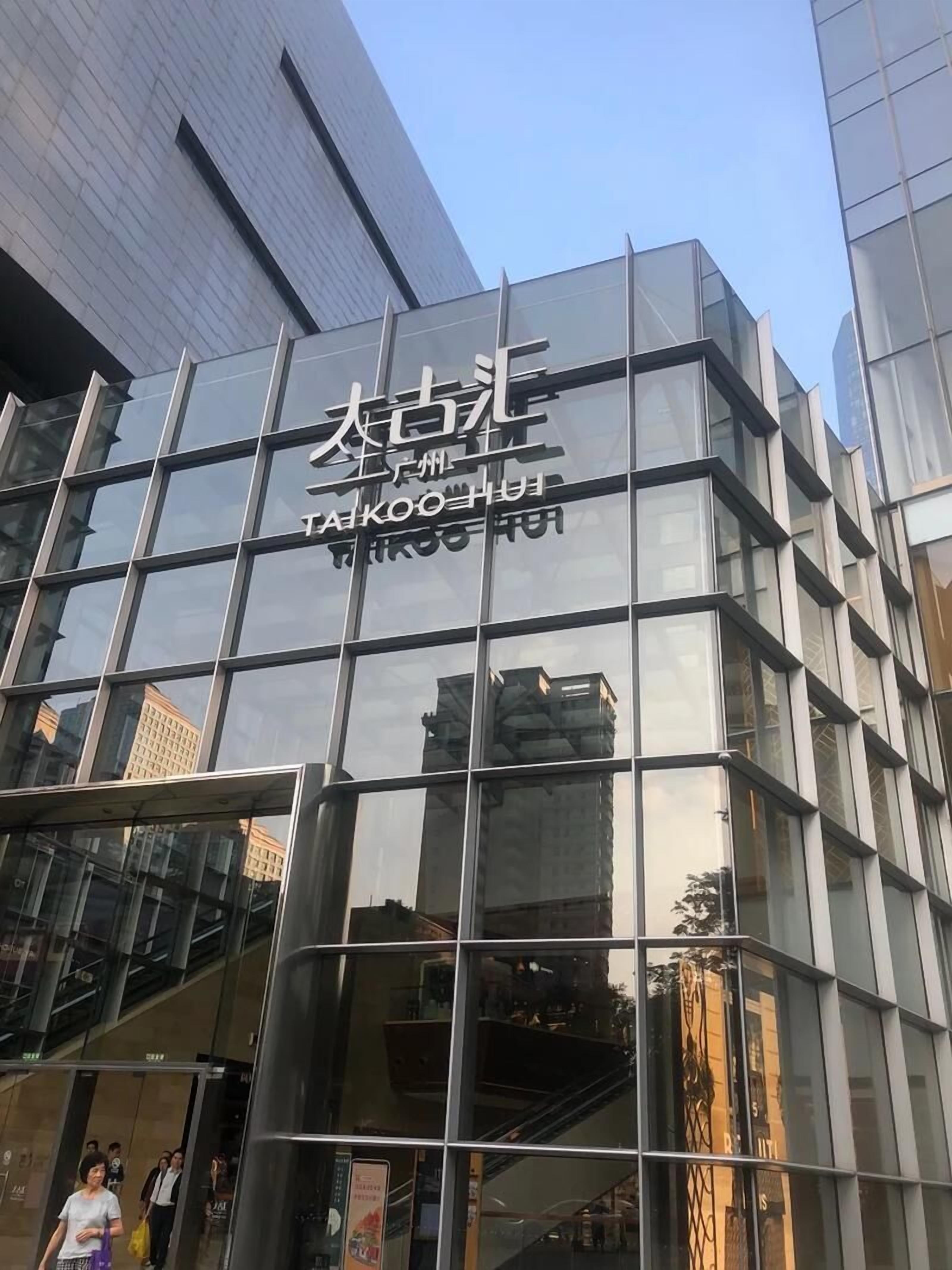 Un bâtiment moderne avec des fenêtres en verre réfléchissant et une enseigne sur laquelle on peut lire « TAKKOO HUI ».