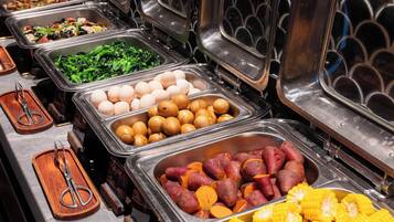 Een buffet met verschillende soorten eten in metalen bakken, zoals groenten, eieren en maïs.