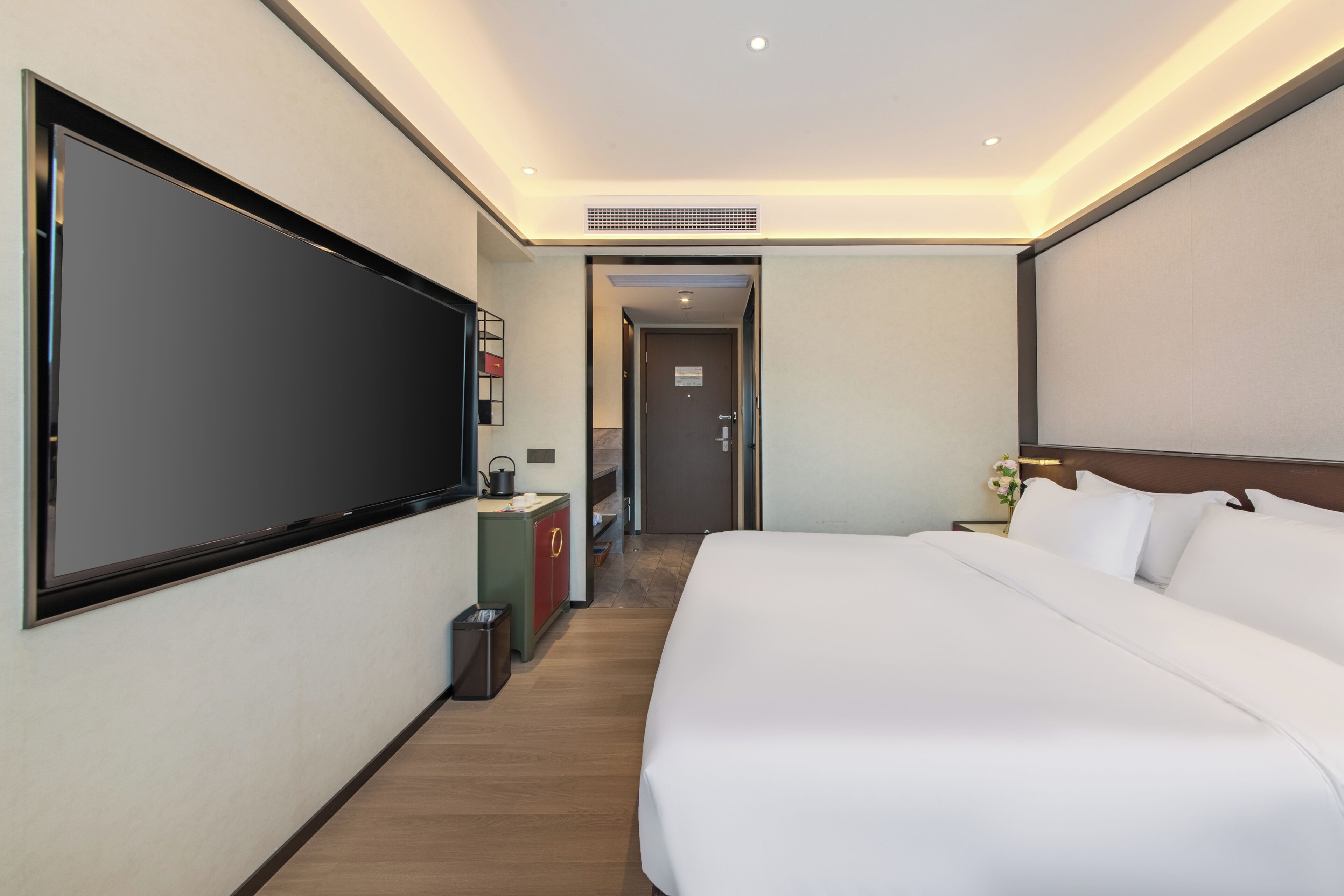 A hotel room with a large bed, a flat-screen TV, a desk with a chair, and a small kitchenette.