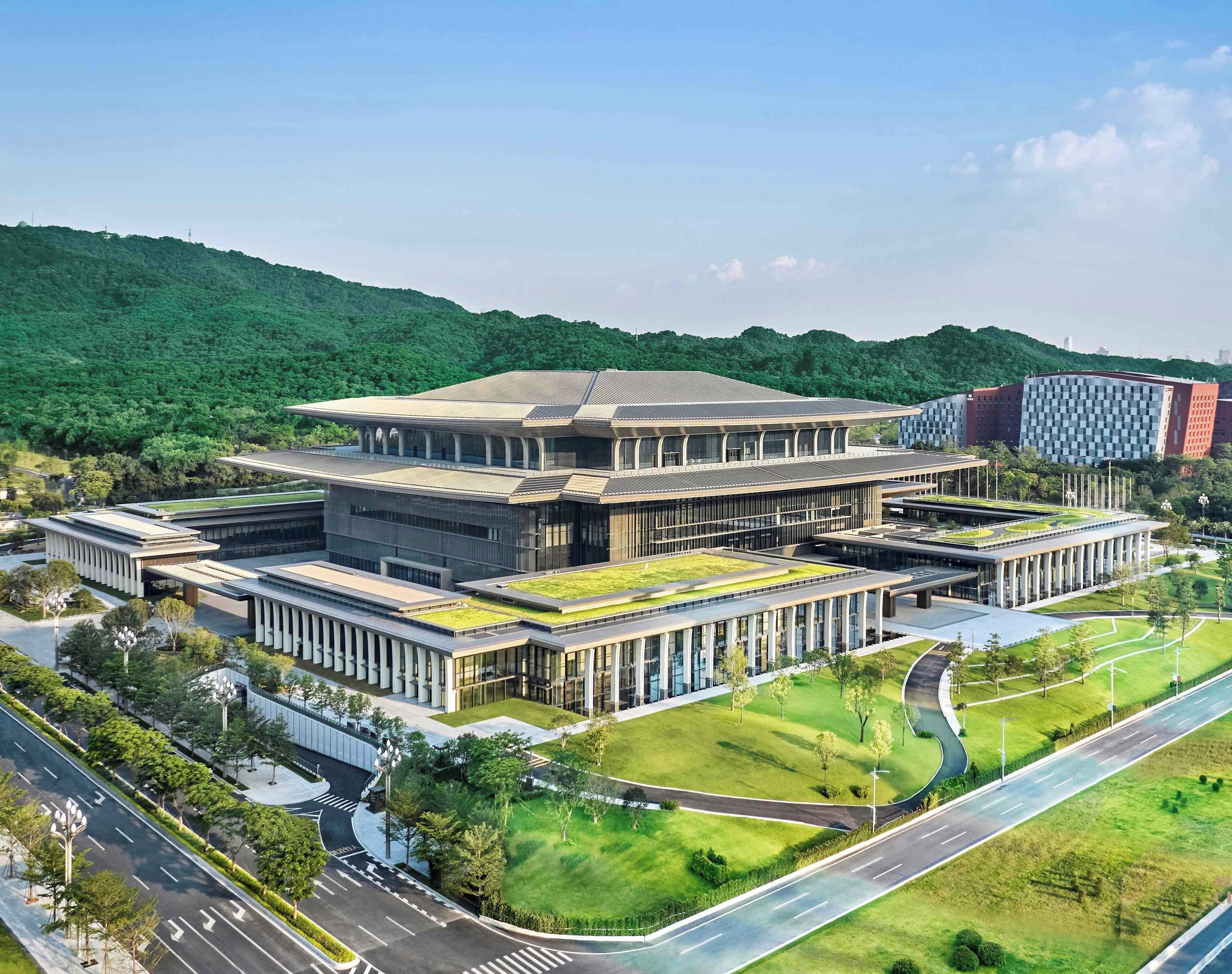 A modern building with a central courtyard, surrounded by greenery and a curved road.