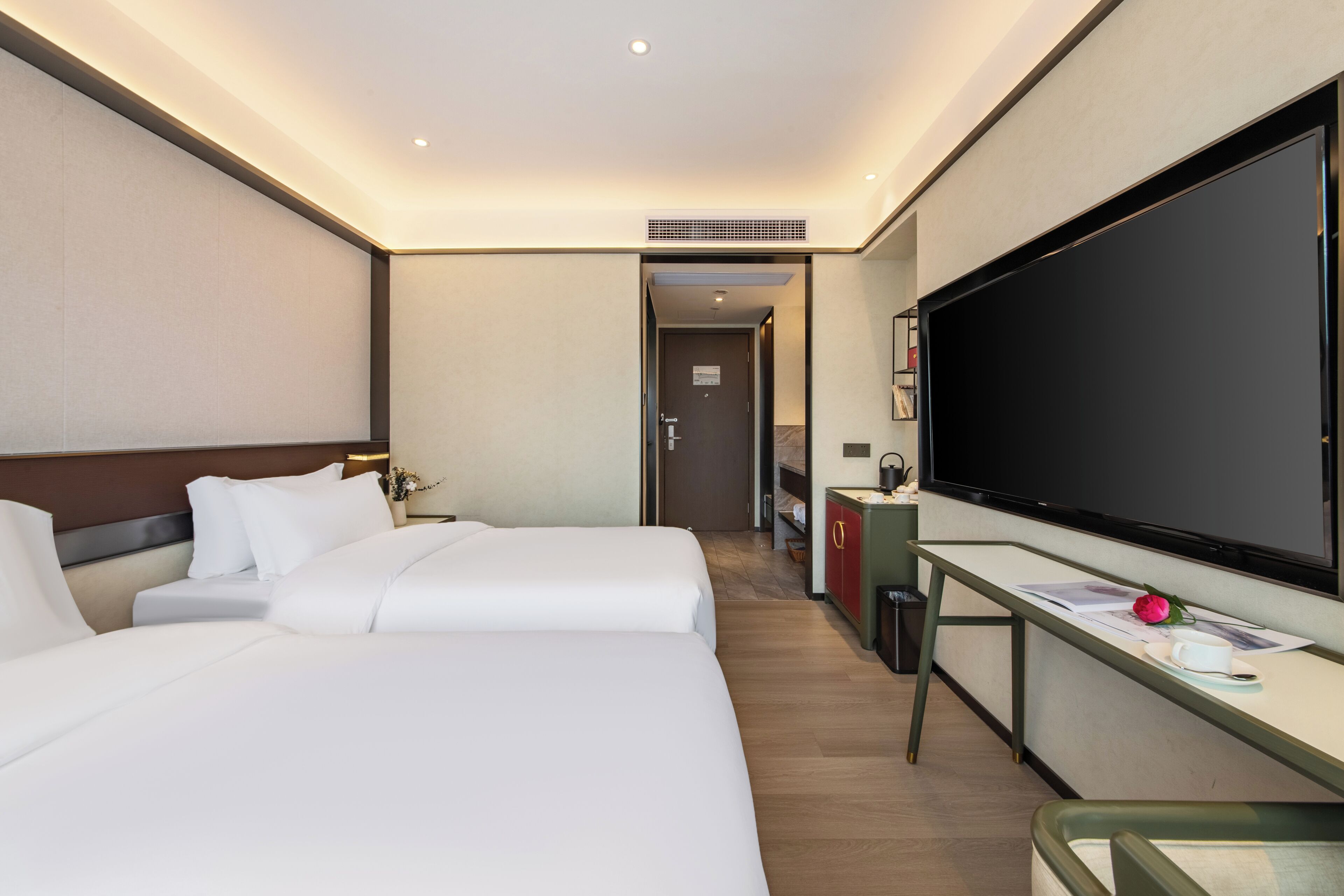 Una camera d'albergo con due letti, una scrivania con televisione a schermo piatto e un angolo cottura.