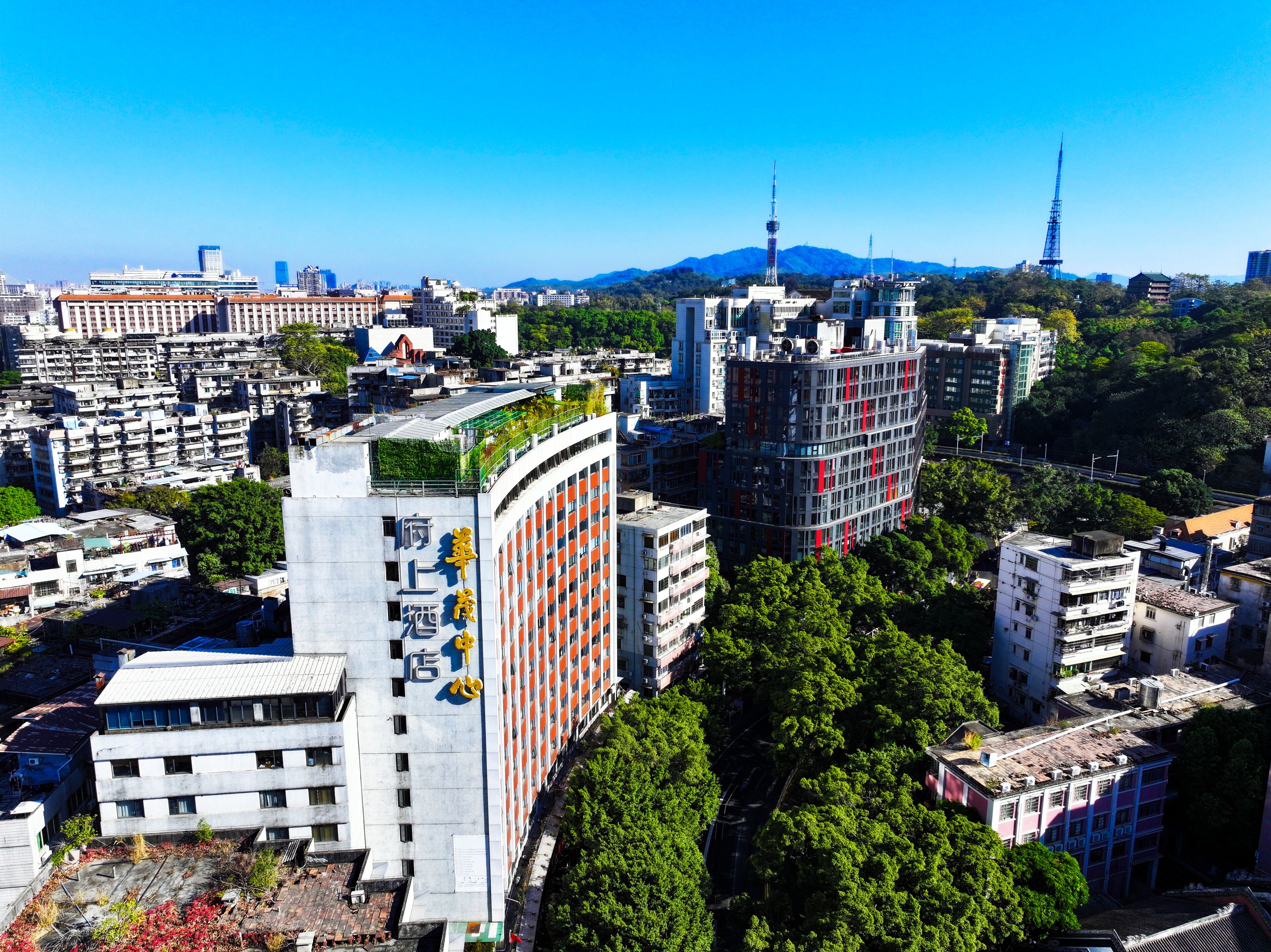 A high-rise hotel with multiple floors, surrounded by dense urban buildings and greenery.