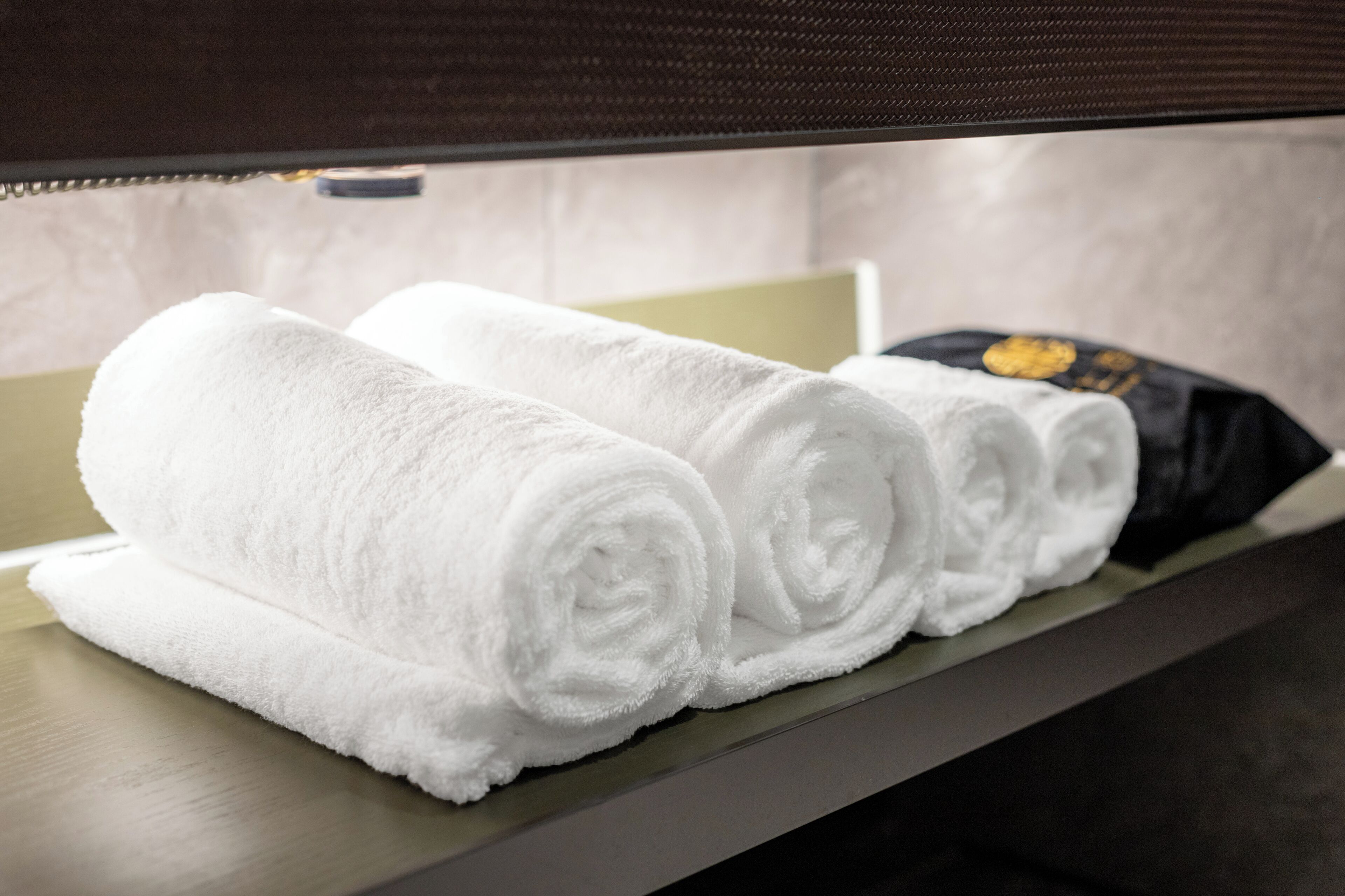 Neatly rolled white towels on a wooden shelf in a hotel room.