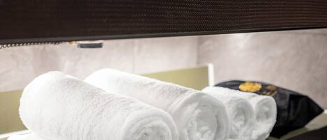 Neatly rolled white towels on a wooden shelf in a hotel room.