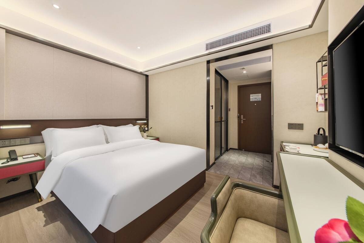 A hotel room with a large bed, bedside table, lamp, and a TV.