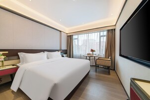 Una camera d'albergo con un letto grande, una scrivania, una sedia, una televisione e una finestra con tende.
