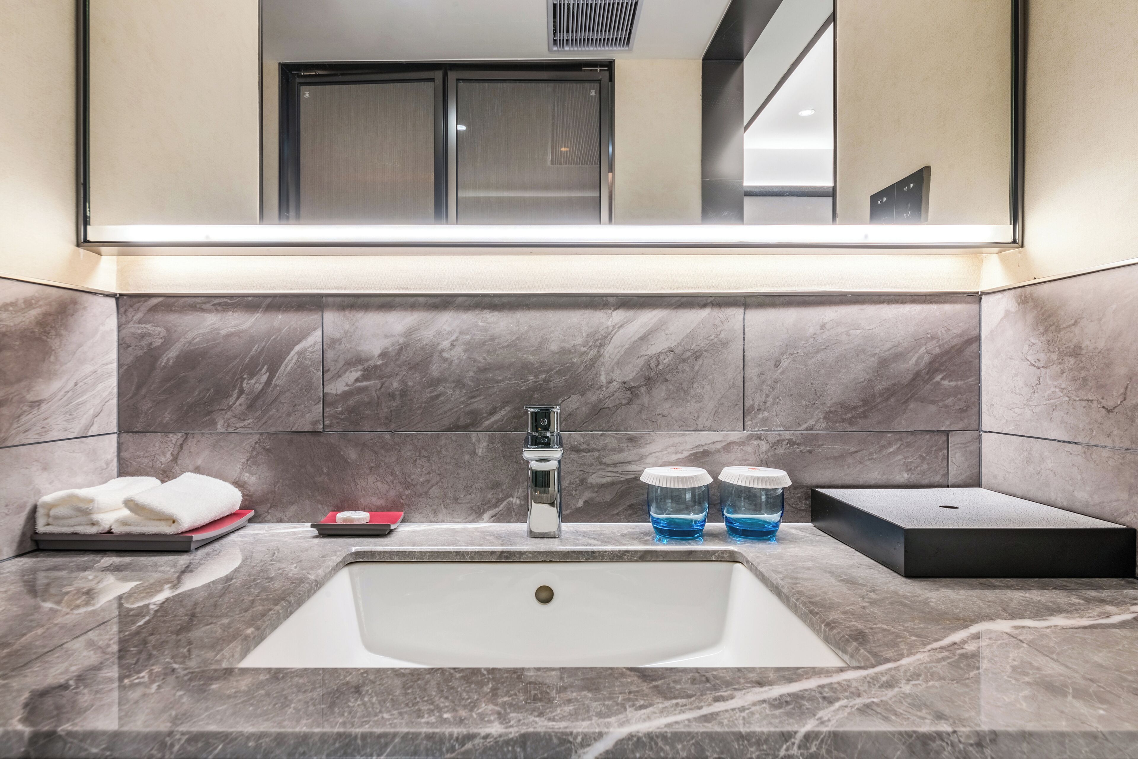 A modern bathroom with a large mirror, a white sink, marble tiles, and a towel rack.
