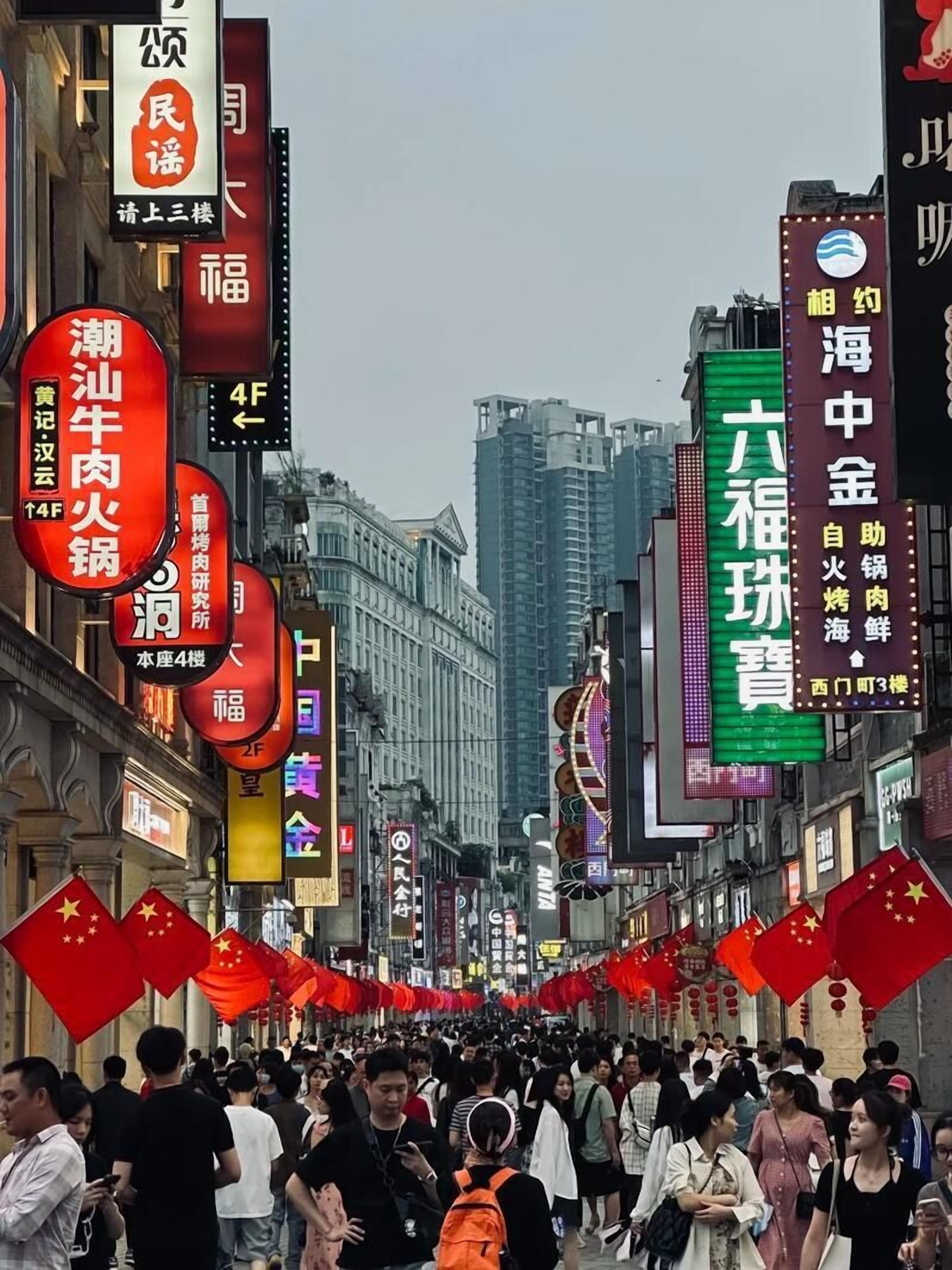 A crowded street lined with traditional Chinese architecture and numerous commercial signs.
