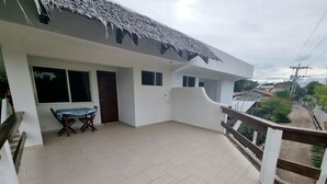 A spacious balcony with a wooden floor, a dining table with chairs, and a thatched roof. - Day & Night Accommodations (Daanbantayan)