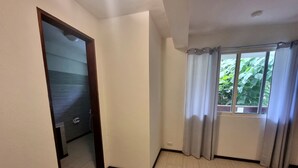 A room with a bed, a window with curtains, a door leading to another room, and a view of greenery outside. - Day & Night Accommodations (Daanbantayan)