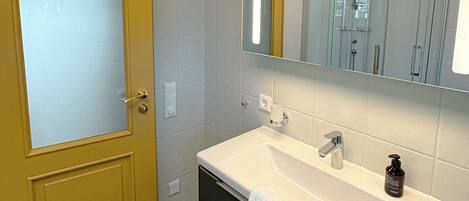 Une salle de bain avec une porte jaune, un lavabo blanc, un miroir et une serviette.