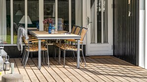 Une terrasse en bois avec une table et des chaises, une porte avec des panneaux de verre et une lanterne.