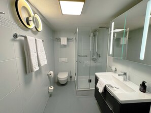A modern bathroom with a glass shower enclosure, a white sink, and a large mirror.