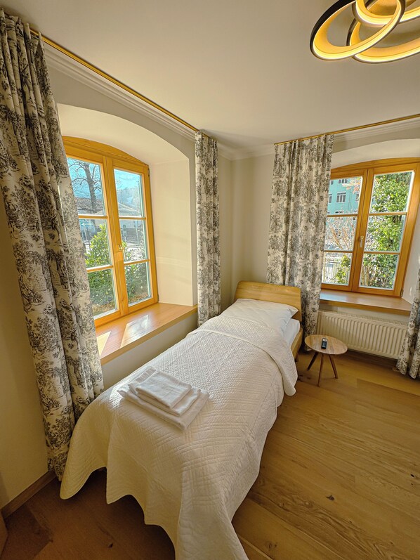 A bedroom with a bed, two windows, a radiator, and a small table.