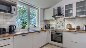 Una cocina moderna con armarios blancos, microondas, hervidor, cafetera y ventana con vistas a árboles.