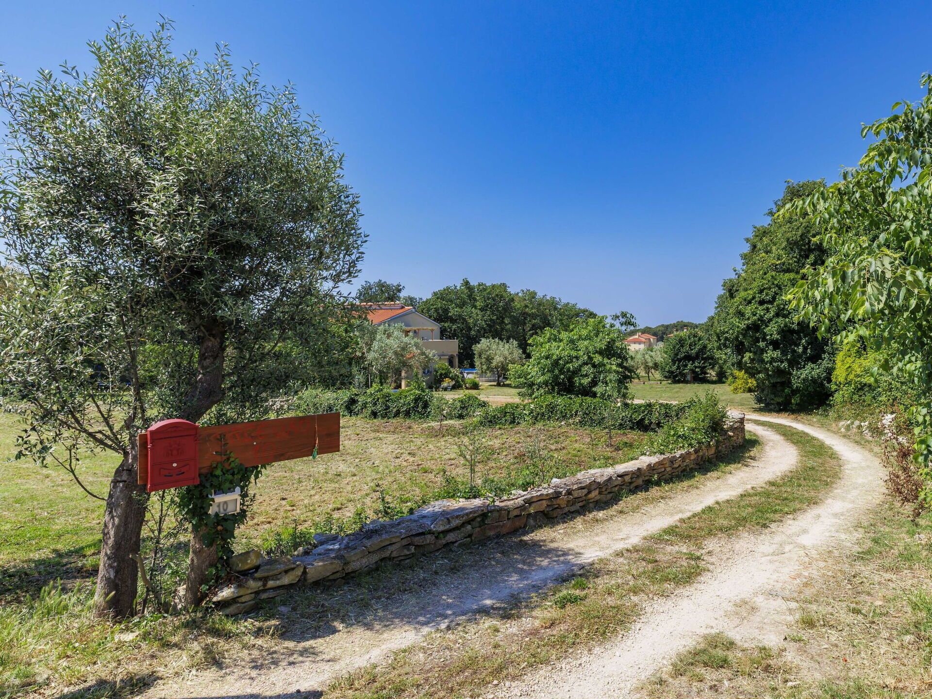 Ländliche Landschaft mit einem Feldweg, einer Steinmauer und einem roten Briefkasten.