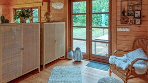 L’intérieur chaleureux d’un chalet, avec un revêtement mural en bois, une grande porte vitrée donnant sur un jardin, des meubles en osier et un globe terrestre posé sur une étagère.