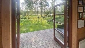 Une porte en bois ouverte donne sur une terrasse d’où l’on peut admirer un espace verdoyant et des arbres.