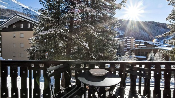 Ein Balkon mit Tisch und Stühlen, mit Blick auf einen verschneiten Berg und eine Stadt.