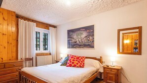 Ein Schlafzimmer mit einem hölzernen Bett, einem Nachttisch, einem Fenster mit Vorhängen, einem Bild an der Wand und einem Spiegel.