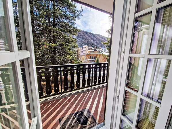 Un balcon donnant sur une colline boisée et sur des bâtiments situés au loin.