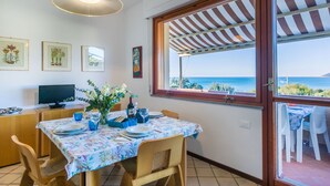 Ein Essbereich mit Tisch für zwei Personen, einem Fernseher und Blick auf das Meer durch ein großes Fenster.