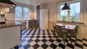 Une cuisine de taille réduite avec un sol à carreaux noirs et blancs, un réfrigérateur blanc et un coin repas comprenant une table et des chaises.