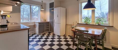 A compact kitchen with a black and white checkered floor, a white refrigerator, and a dining area with a table and chairs.