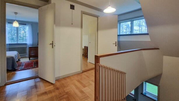 Une pièce spacieuse avec un plancher en bois, un lit, une commode et une fenêtre donnant sur des arbres.